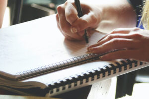 A person drinking coffee and writing in a notebook.