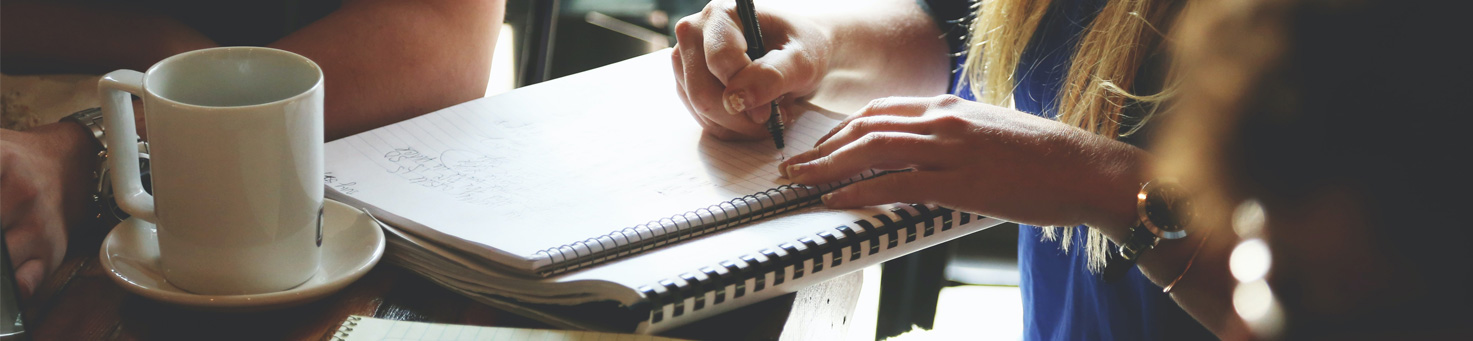A person drinking coffee and writing in a notebook.
