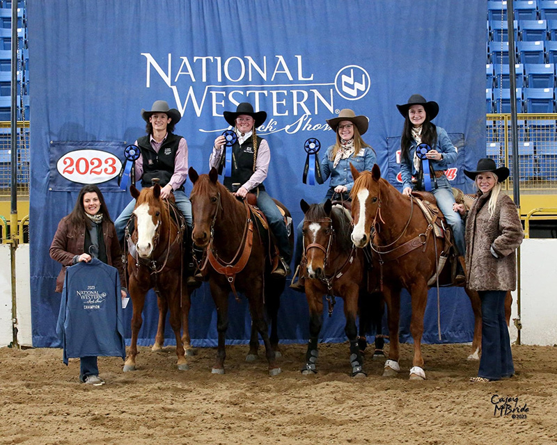 Rodeo team holding up awards while saddled on horses.
