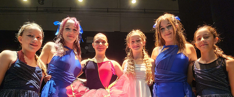 6 young women in dance costumes pose for a photo.