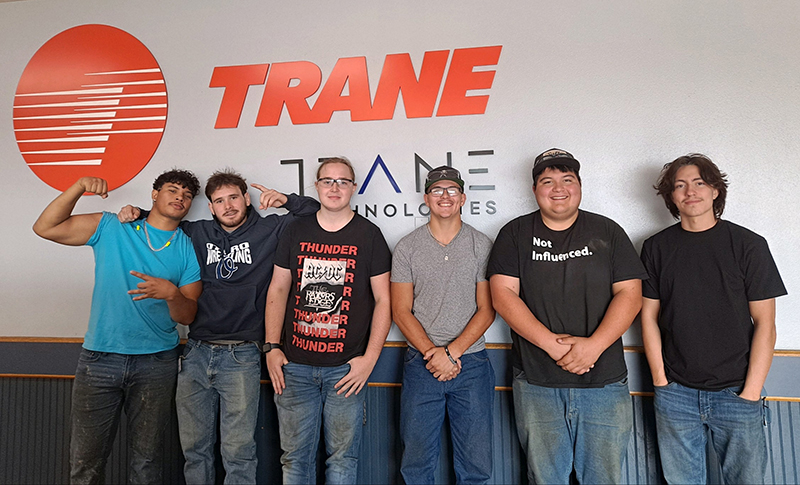 A group of students stands in front of the TRANE logo