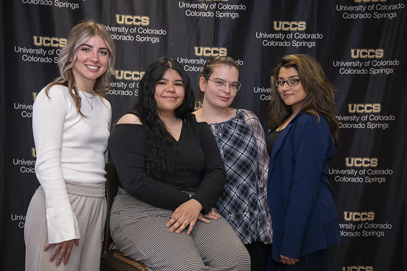 4 women pose for a photo in front of a UCCS backdrop.