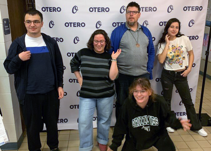 A group of students pose in front of a background with repeating O's and Otero College Logos on it.